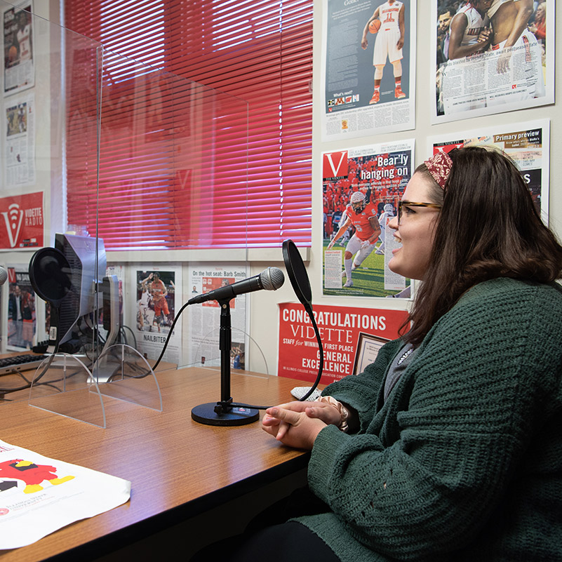 Two women sitting at a desk, speaking into a microphone.